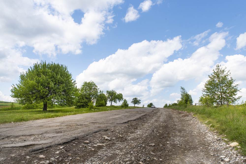 Poorly maintained paved road with asphalt crumbling to travel to homestead property.